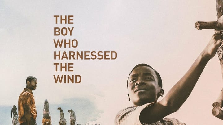 Film poster for The Boy Who Harnessed the Wind: a Malawian boy raises his arm beside a handmade windmill, with villagers in the background and the title text on the left.